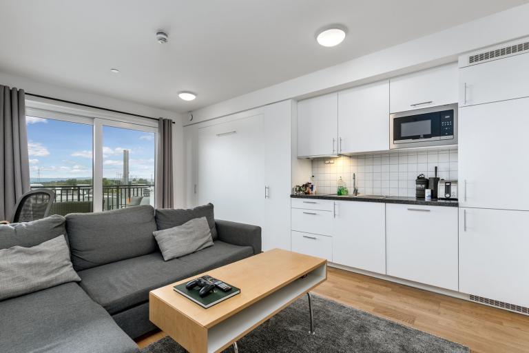 Stuen fremstår som svært innbydende i lyse, delikate fargevalg. På gulvet er det lagt trestavs eikeparkett som strekker seg sømløst gjennom leiligheten.